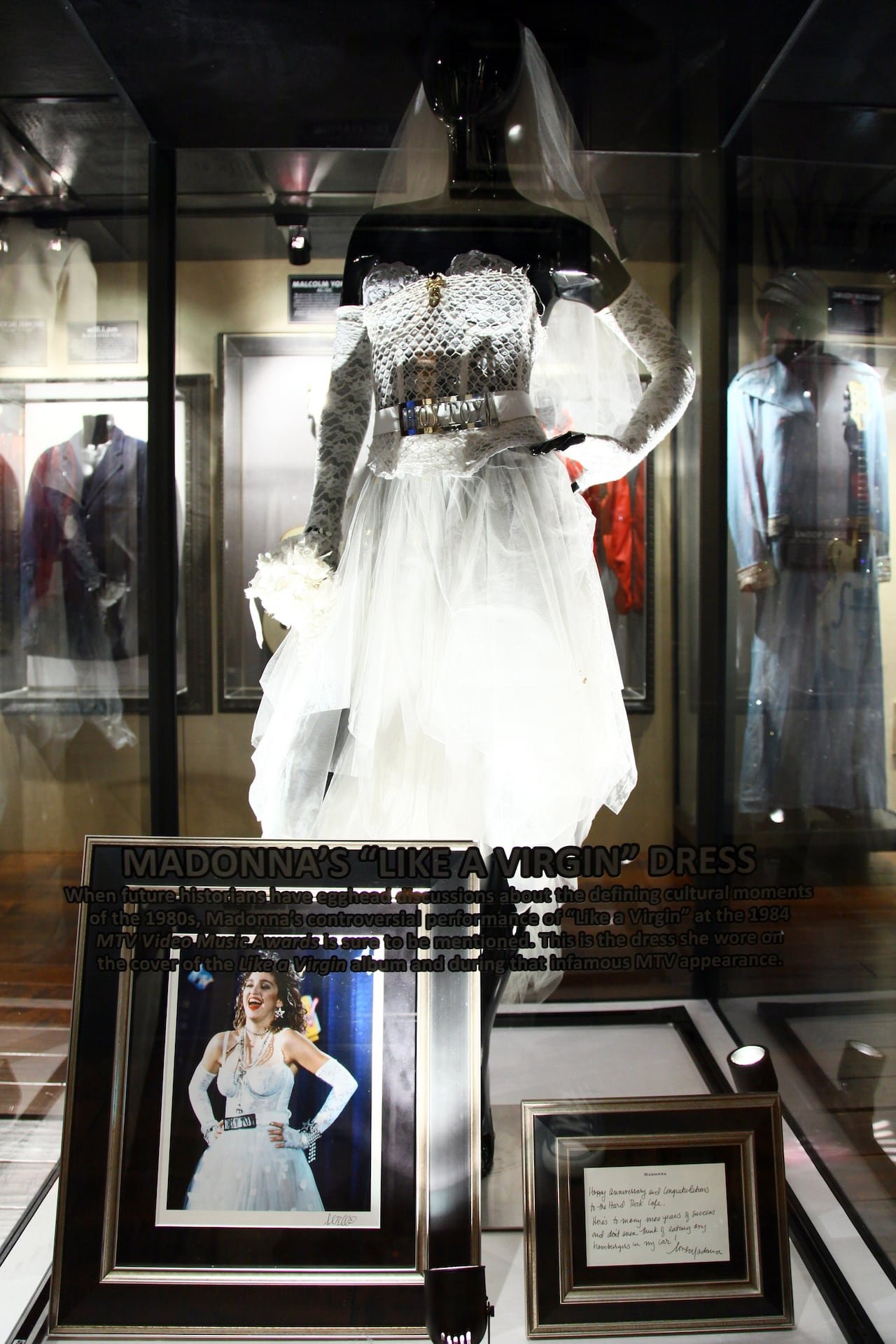 default-1438 A wedding dress and a belt reading "Boy Toy" displayed in a case on a mannequin. A photo of a woman wearing the dress and a plaque sit in front of it.