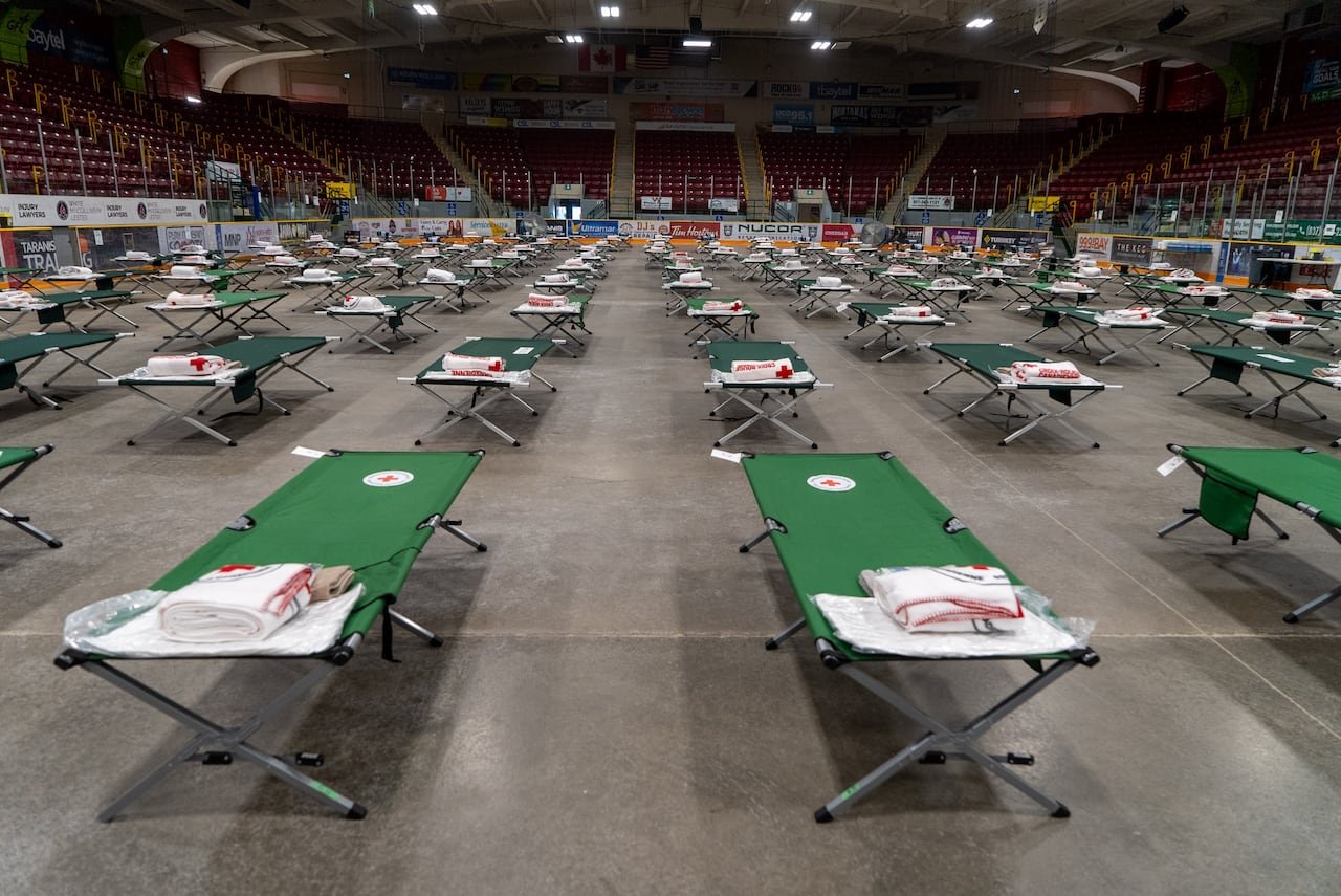 default-1444 Dozens of green cots are set up on the concrete floor of an arena.