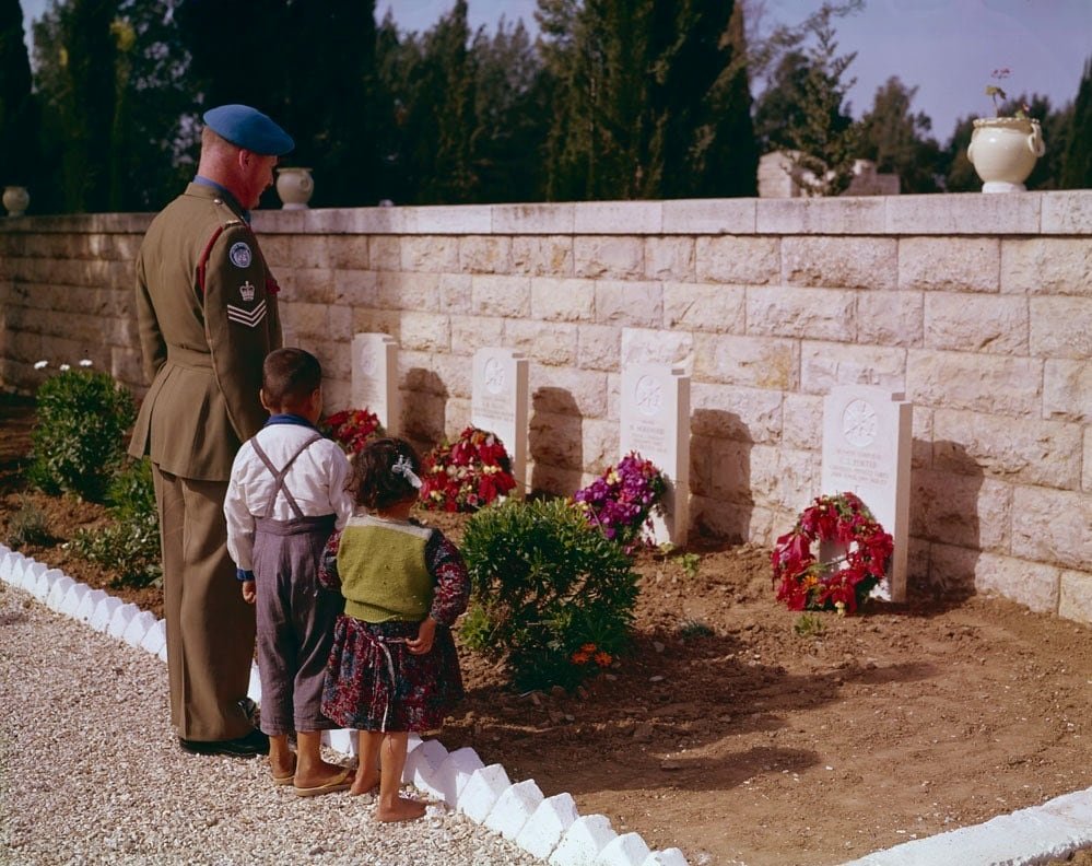A soldier in a blue UN beret and two young children view a row of headstones.