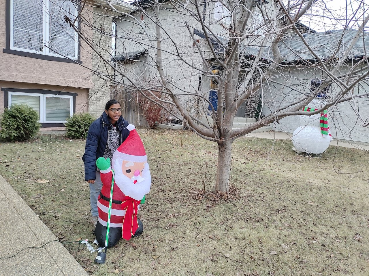 default-355 A girl in glasses stands behind an inflatable Santa Claus on a lawn devoid of snow in winter.