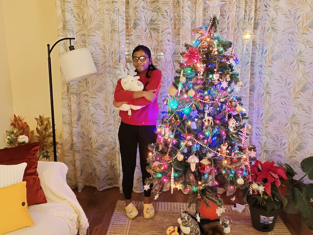default-356 A girl cuddles a stuffed animal standing beside a brightly lit Christmas tree.