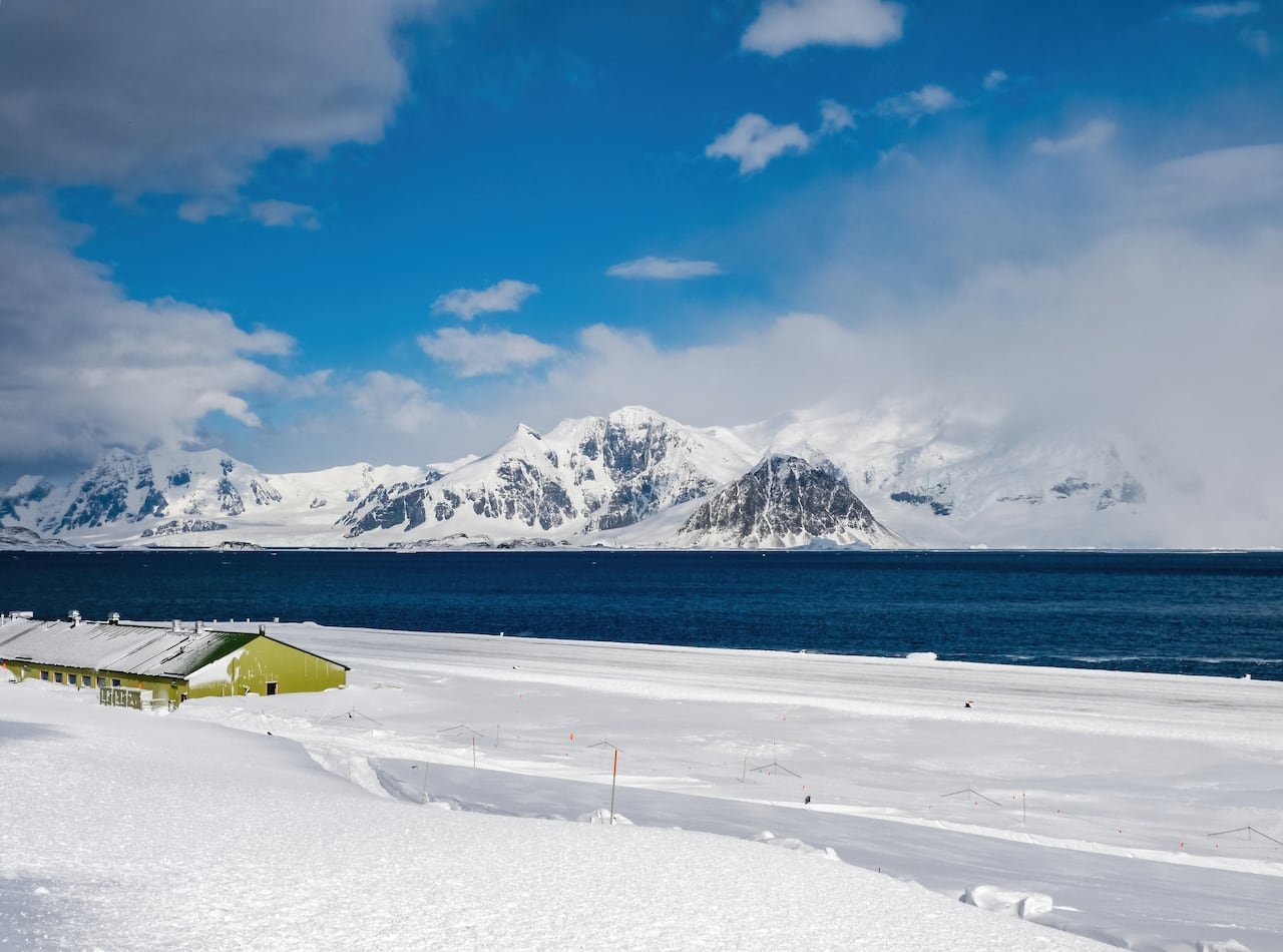 default-620 A low green building, half buried in snow, next to a lake with snowy mountains on the horizon