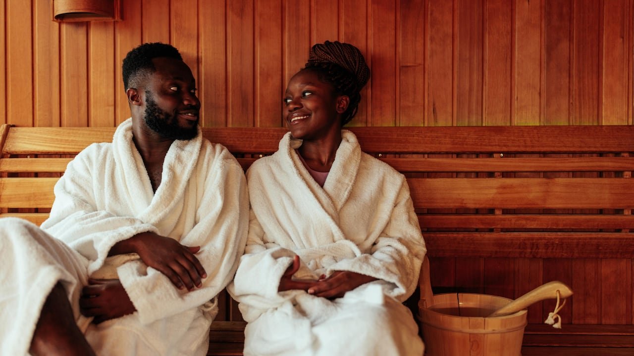default-542 A couple in bath robes sitting in a sauna, smiling at each other.